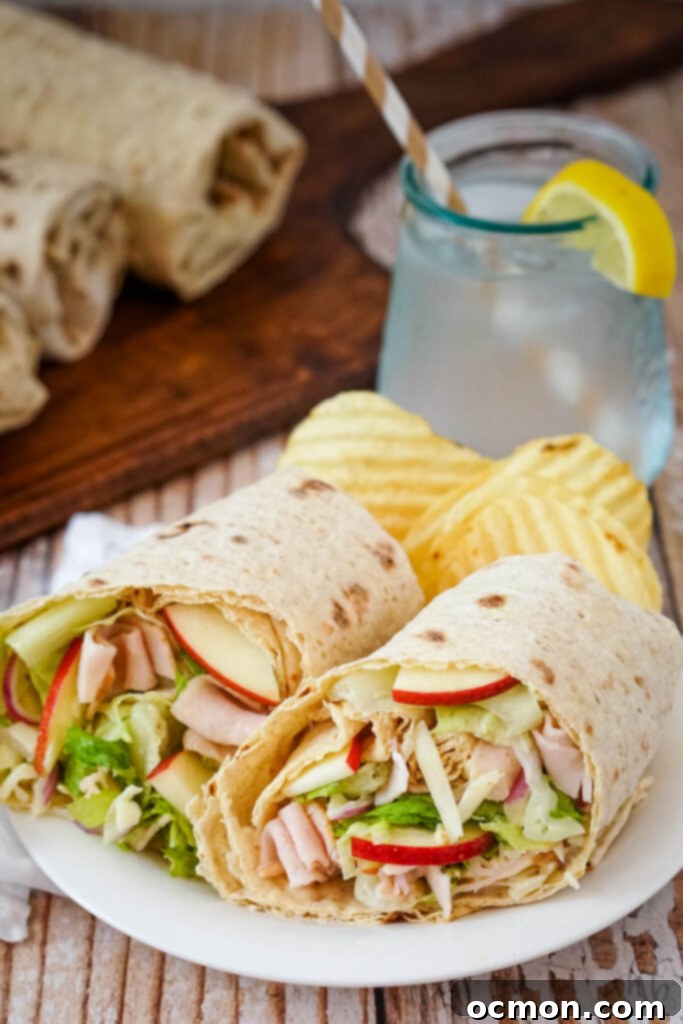 A Turkey Swiss and Apple Wrap cut in half and served with potato chips on a white plate.
