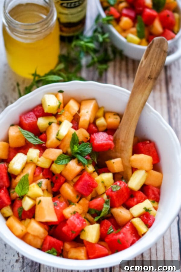 A white bowl of the finished watermelon fruit salad sitting next to a jar of honey and a bottle of balsamic vinegar.