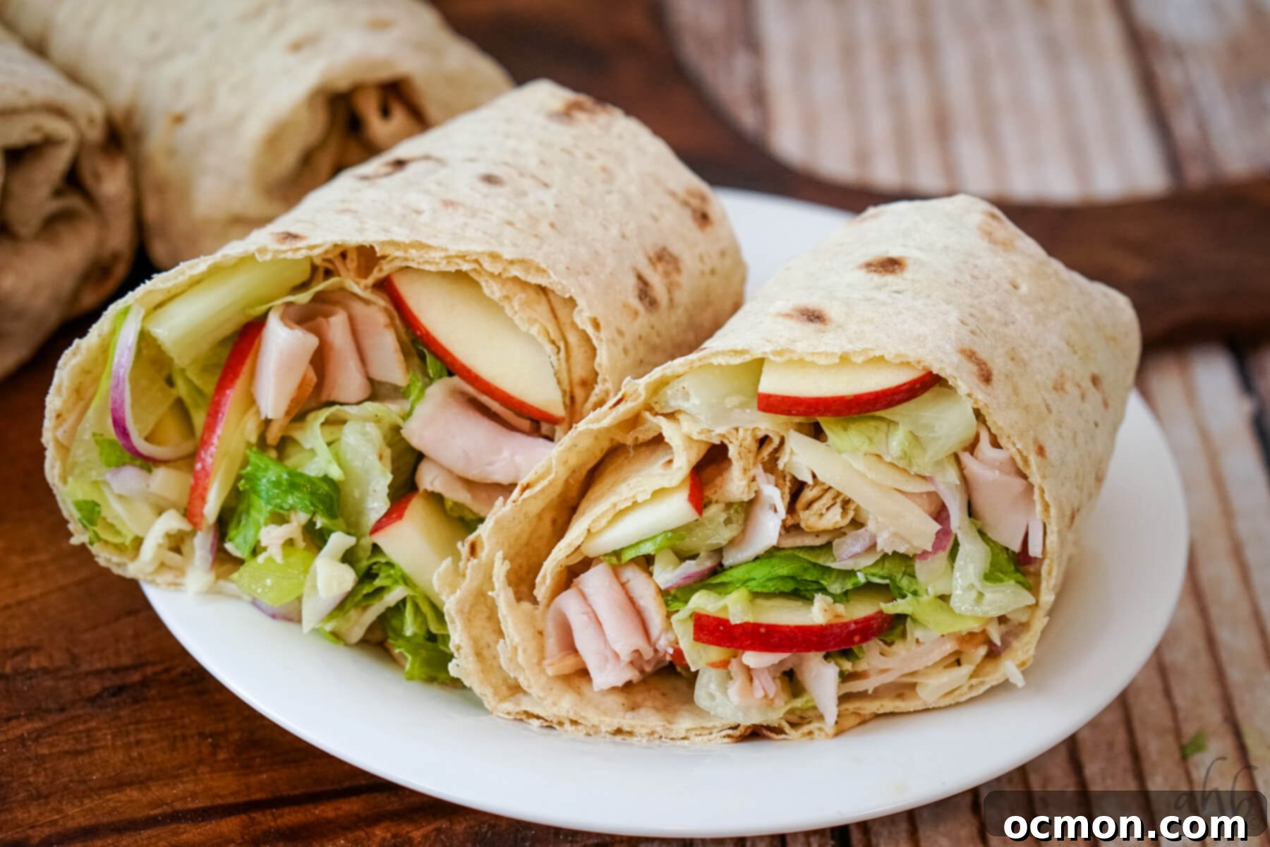 A complete Turkey Swiss and Apple Wrap cut in half and served on a white plate.
