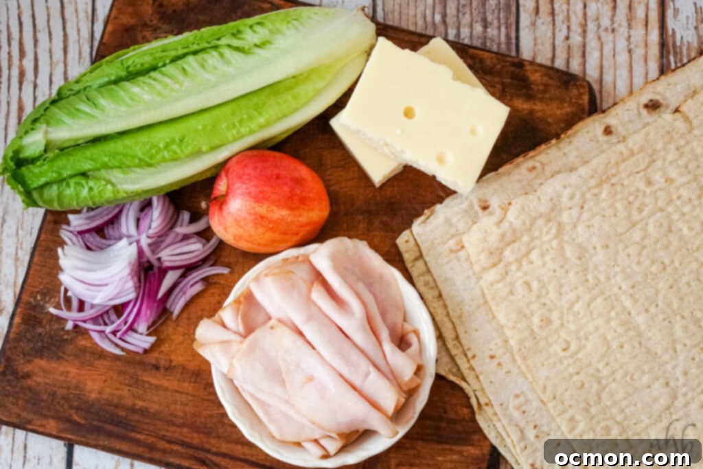 A head of romaine lettuce, a red apple, two blocks of swiss cheese, thinly sliced red onion, sliced turkey, and four large tortillas on a wooden cutting board.