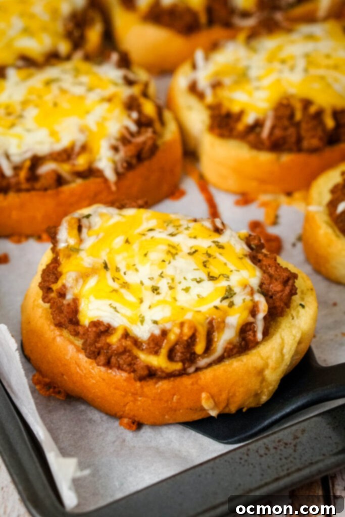 Sloppy Joe Stuffed Garlic Bread 3 A black spatula scooping a cheesy Garlic Bread Sloppy Joe from a baking sheet, showcasing the melted cheese and hearty beef filling.