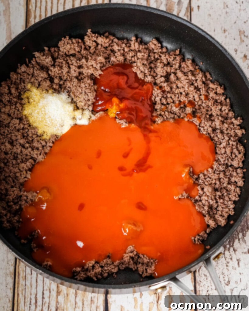 Sloppy Joe Stuffed Garlic Bread 6 Browned ground beef in a black skillet with condensed tomato soup, ketchup, Worcestershire sauce, yellow mustard, onion powder, salt, and garlic powder added.