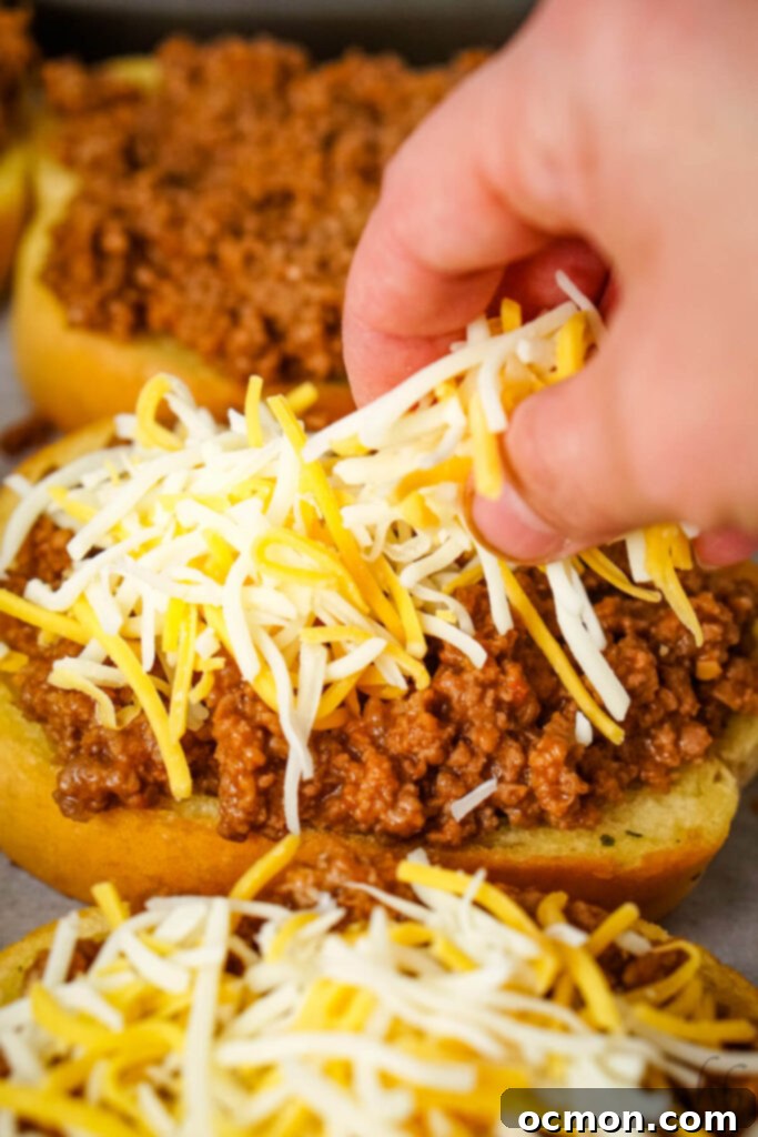 Sloppy Joe Stuffed Garlic Bread 8 Shredded Colby Jack cheese being sprinkled over the garlic bread slices topped with sloppy joe meat, ready for melting.