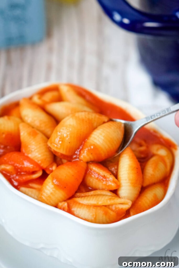 A serving of Old Fashioned Tomato Macaroni in a white bowl being scooped with a spoon.