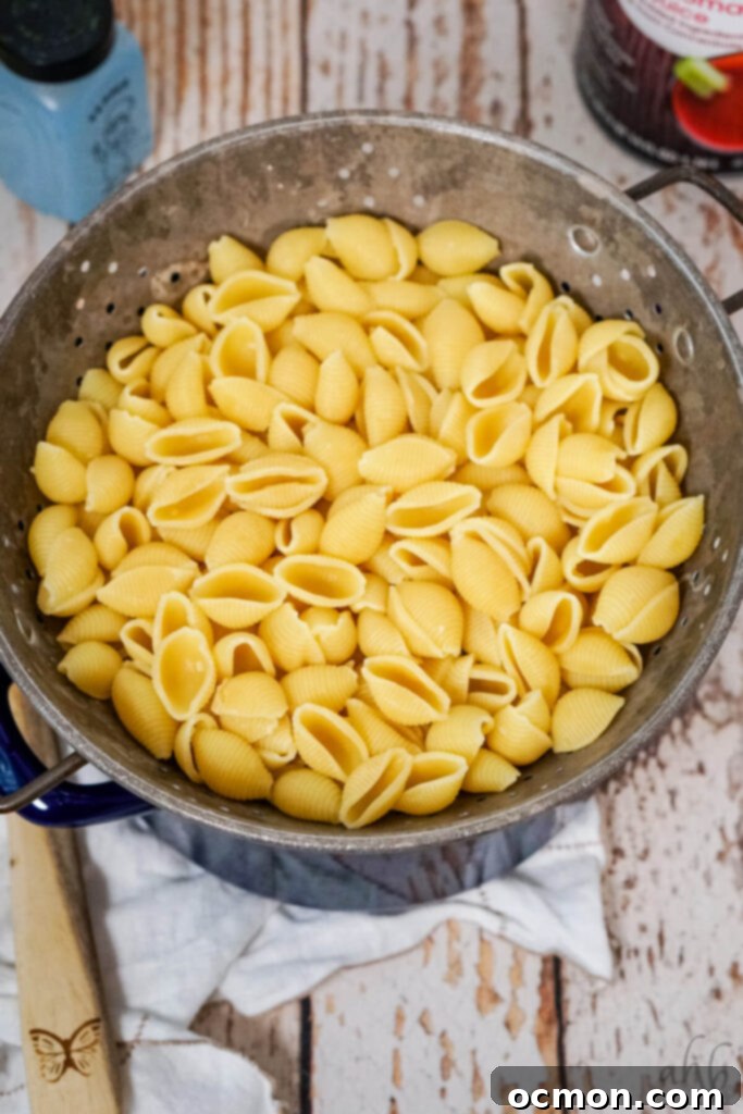 Boiled and drained shell pasta in a colander resting on top of a blue stockpot, ready for the next step.