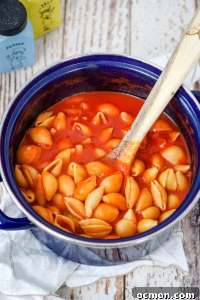 The seasoned Old Fashioned Tomato Macaroni is stirred with a wooden spoon in a blue stockpot, ready for serving.