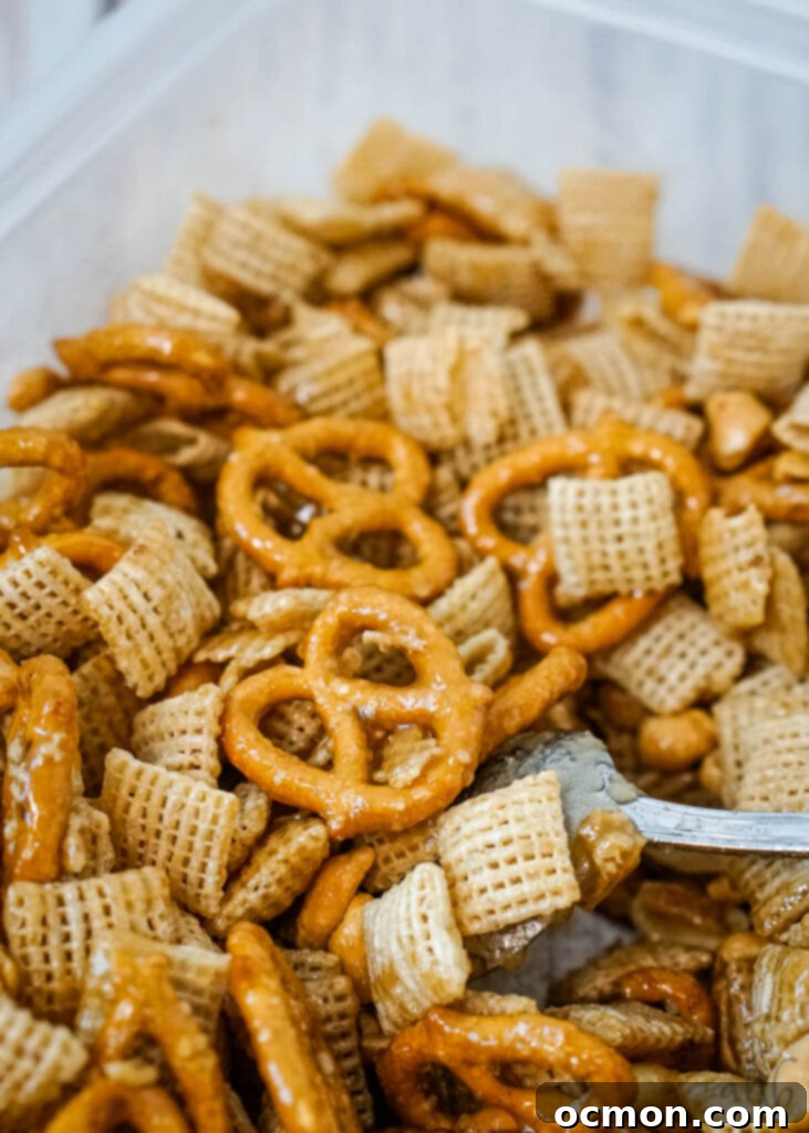 Caramel Apple Crunch Mix 4 A mix of Chex cereal, pretzels, and peanuts covered in the butter and brown sugar mixture being stirred by a spoon, before the apple and caramel additions.
