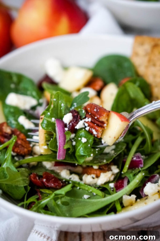A close-up shot of a forkful of Apple Feta Spinach Salad, showcasing crisp apples, green spinach, creamy feta, and toasted pecans. 