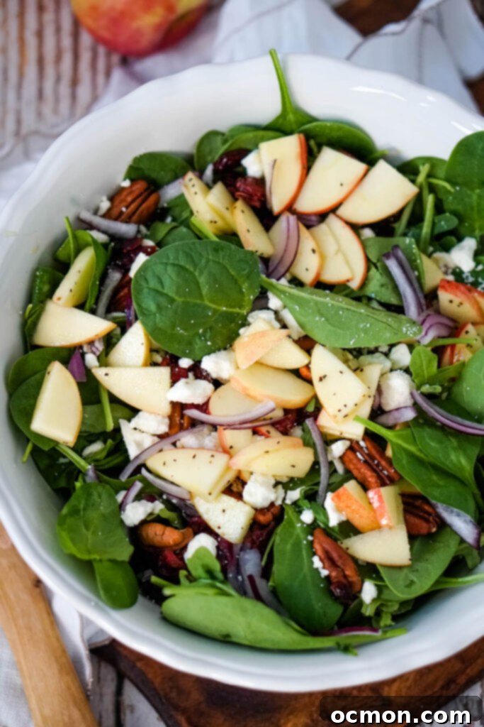 A large white bowl generously filled with a vibrant Apple Feta Spinach Salad, perfectly mixed and ready to serve. 