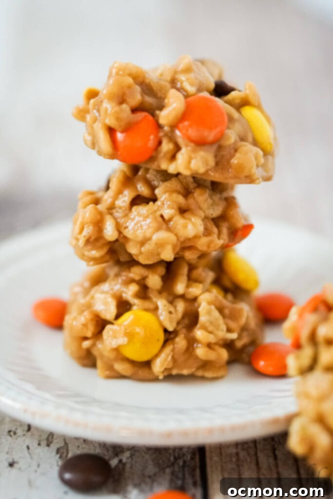 A stack of 3 no bake rice krispies cookies with reeses pieces on a white plate. 