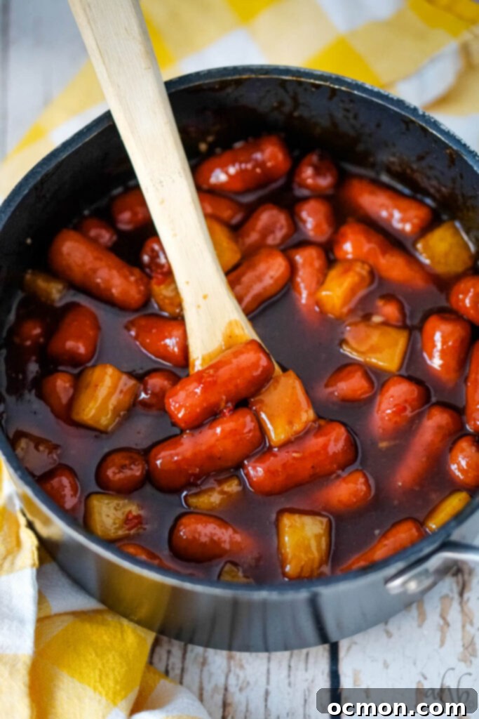 Aloha Smokies 2 A pot of Hawaiian Lit'l Smokies stirred with a wooden spoon, showcasing the rich sauce and pineapple chunks.