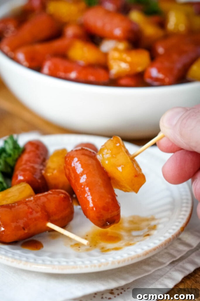 Aloha Smokies 4 Individual toothpick skewers featuring Hawaiian Lit'l Smokies and a juicy pineapple chunk, arranged on a white plate for elegant serving.