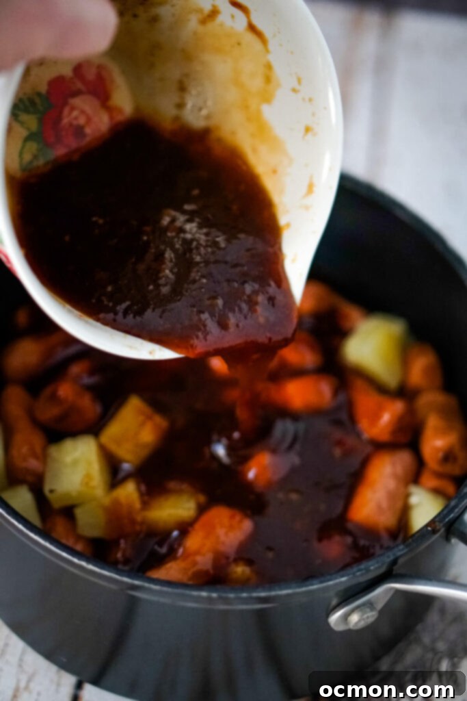 Aloha Smokies 7 The prepared sauce mixture is generously poured over the drained Lit'l Smokies and sweet pineapple chunks in a saucepan, ensuring even coverage.