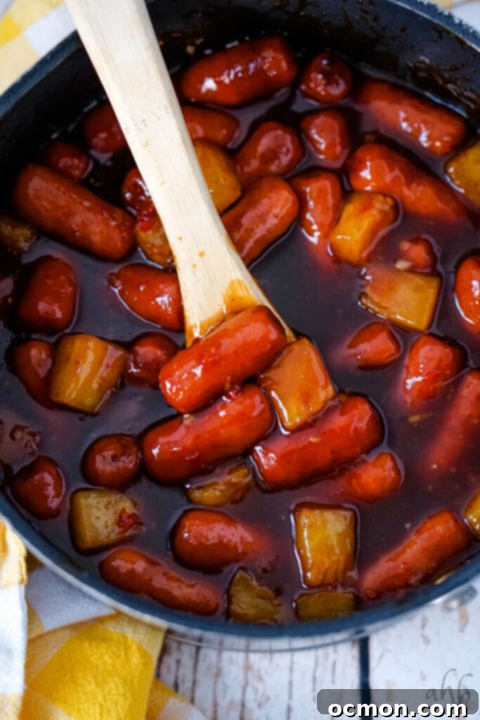 Aloha Smokies 8 A pot of Hawaiian Lit'l Smokies being stirred with a wooden spoon, simmering gently on the stovetop as the sauce thickens and flavors meld.