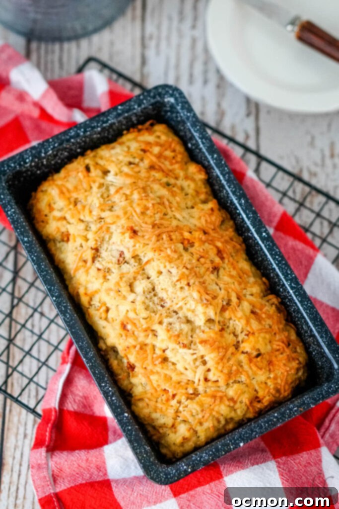 A freshly baked loaf of Sun Dried Tomato and Parmesan Beer Bread is cooling in its pan, emitting a warm, inviting aroma.