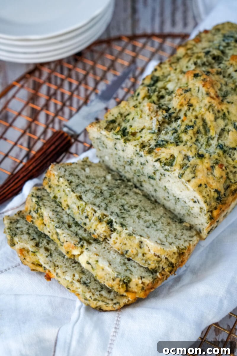 A whole loaf of Spinach and Feta Beer Bread on a towel with three slices already cut and visible, ready for serving.