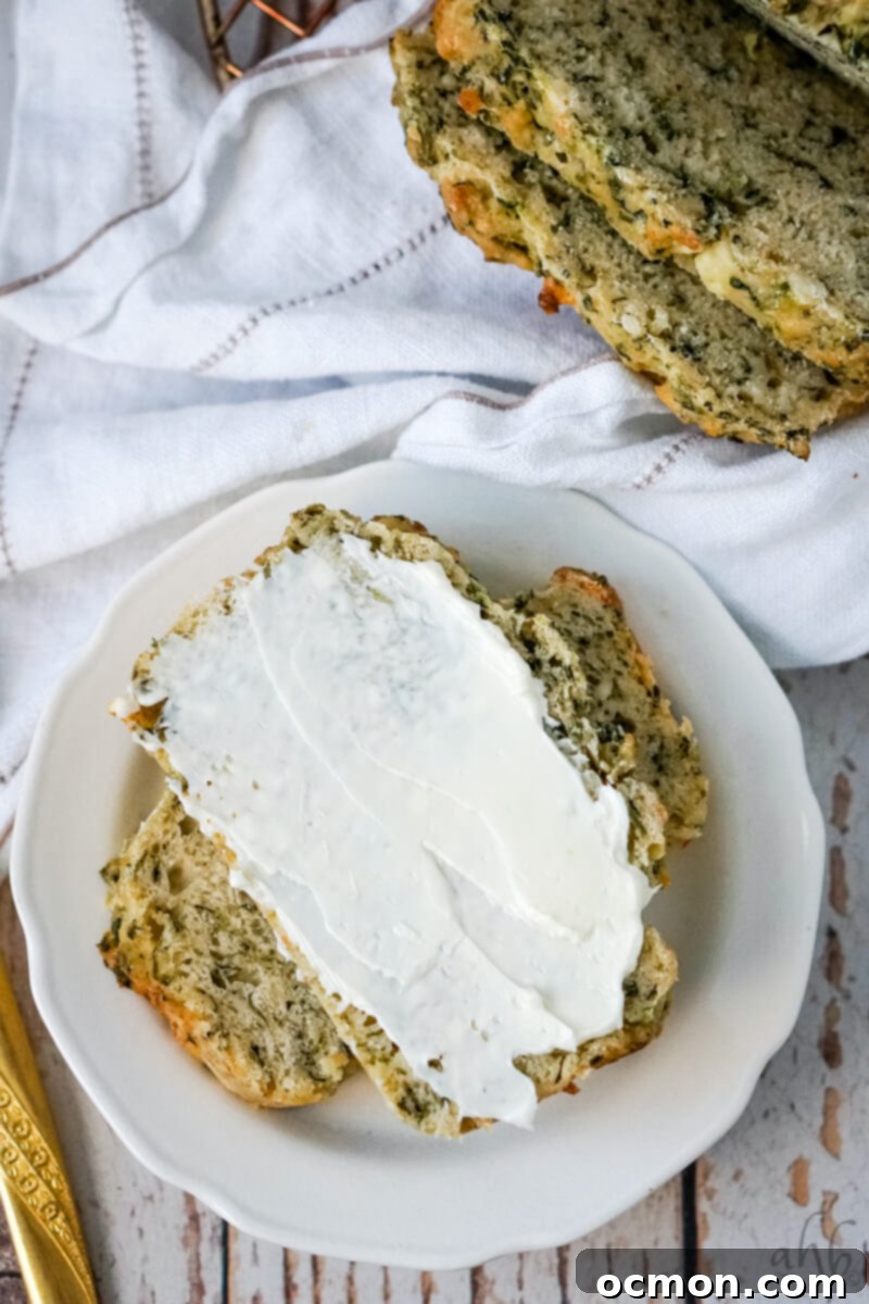 Two slices of warm Spinach Feta Beer Bread on a white plate, ready to be served, with cream cheese spread.