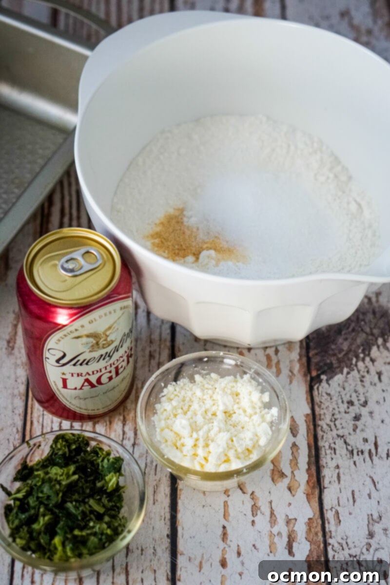A collection of ingredients for Spinach Feta Beer Bread, including a bowl of dry ingredients, a can of beer, a bowl of feta, and a bowl of spinach.