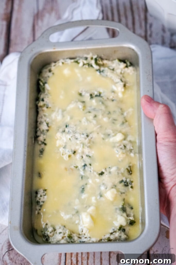 The spinach feta beer bread batter spread into a loaf pan with melted butter being poured evenly over the top.