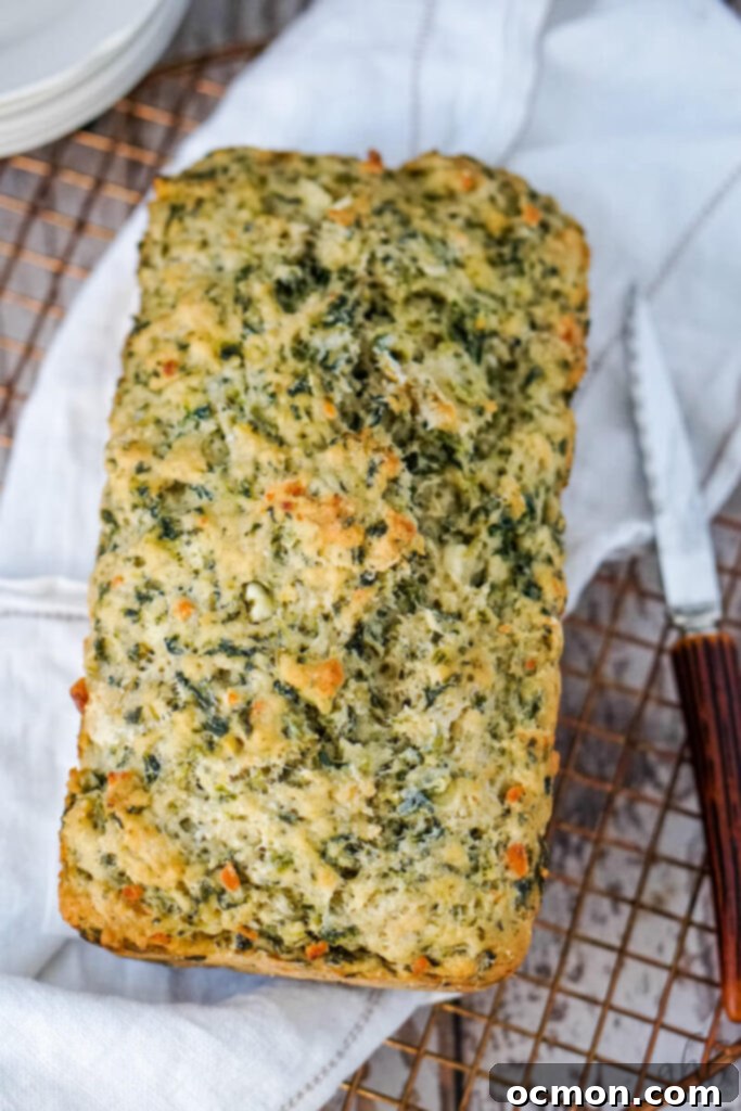 A freshly baked golden brown loaf of Spinach Feta Beer Bread cooling on a wire rack after being turned out of the pan.