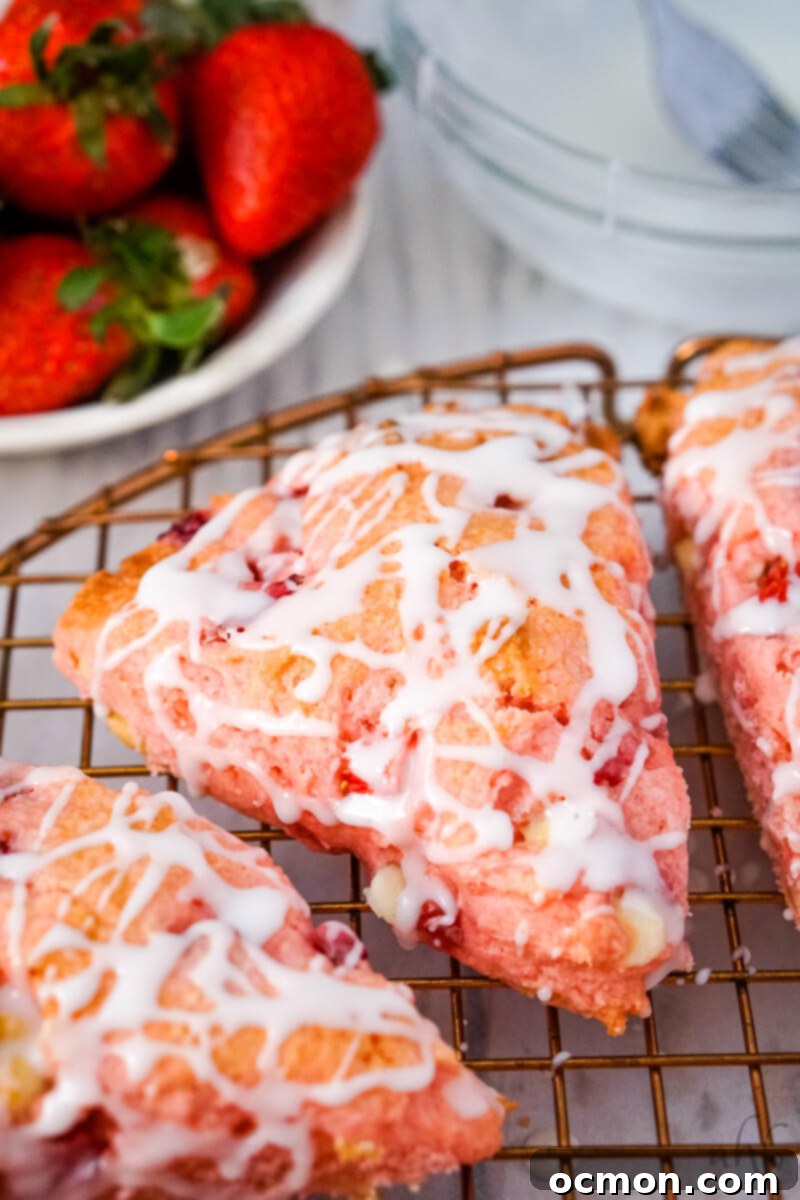 Strawberry Cake Scone Magic 2 A close up image of a strawberry cake mix scone on a wire rack with fresh strawberries in the background.