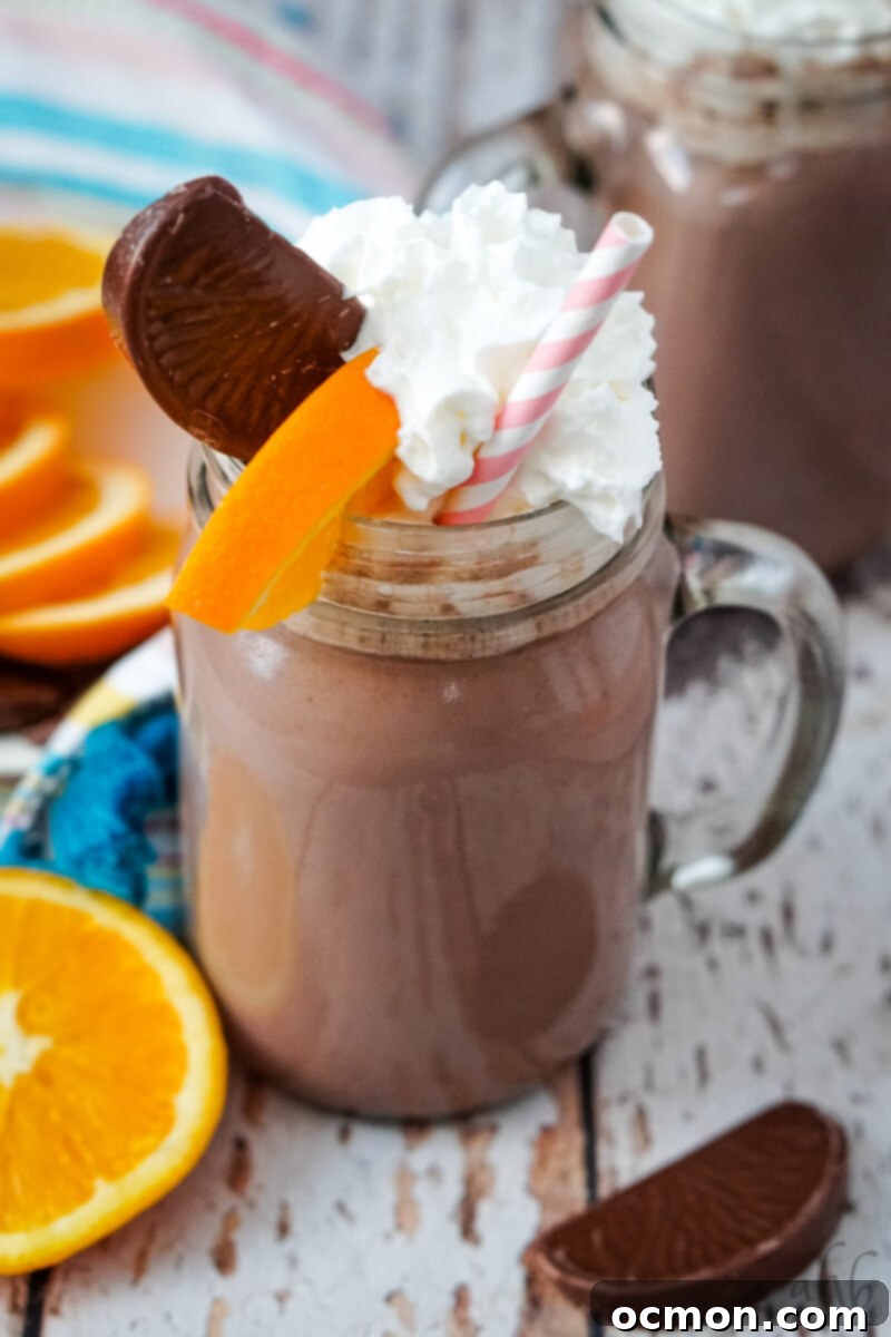 A mug of Orange Hot Chocolate garnished with whipped cream, a slice of Terry's chocolate orange, and a slice of orange. 