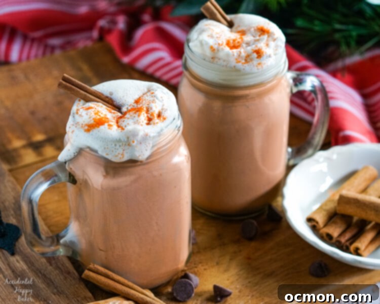 Clear glass mugs of Mexican Hot Cocoa topped with whipped cream and cinnamon sticks on a wooden tray.