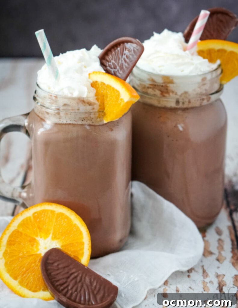 Clear glass mugs full of orange hot chocolate with striped straws in them. An orange and a chocolate in front of the mugs. 