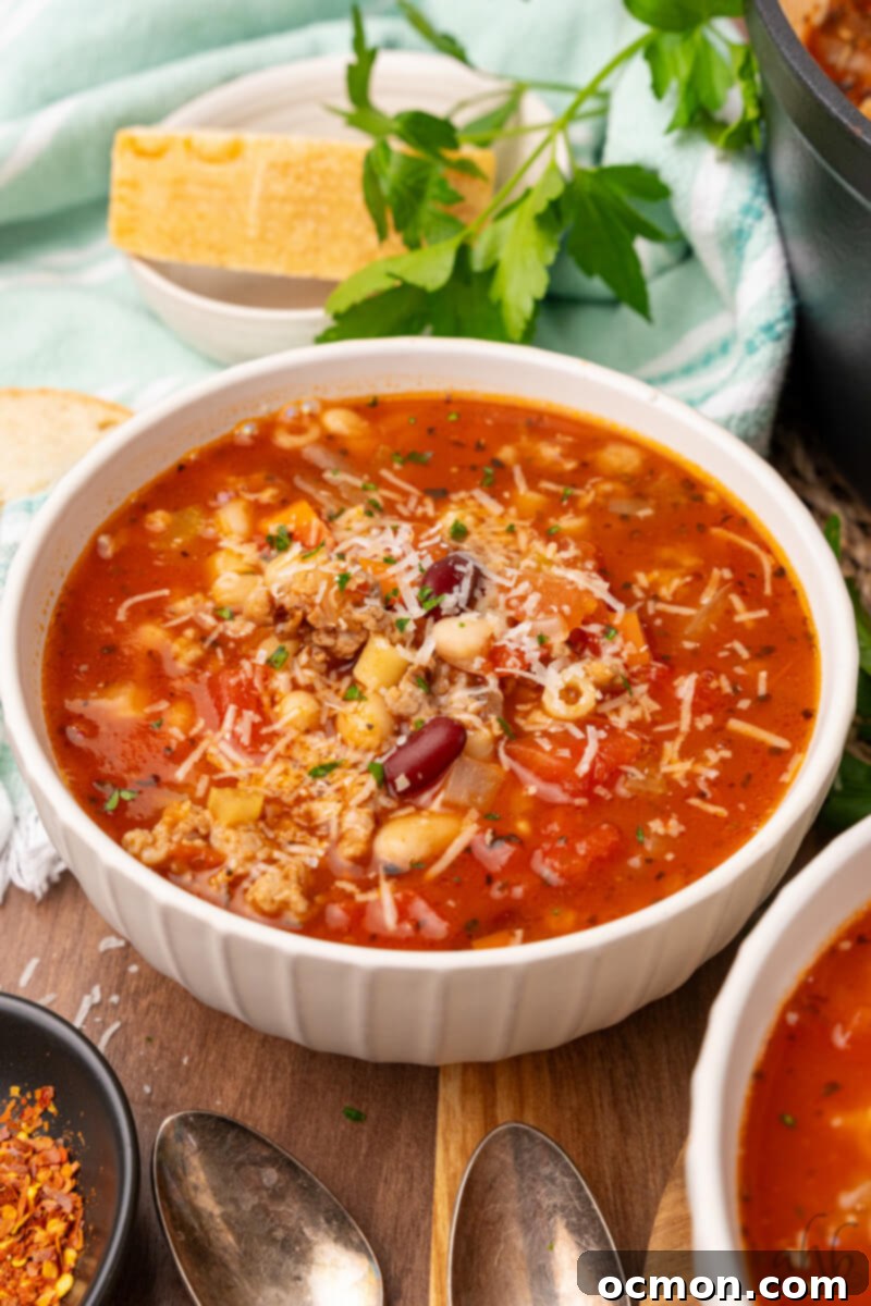 Effortless Sausage Pasta Fagioli 10 A bowl of Easy Pasta Fagioli soup is served in a white bowl and topped with shredded Parmesan cheese.