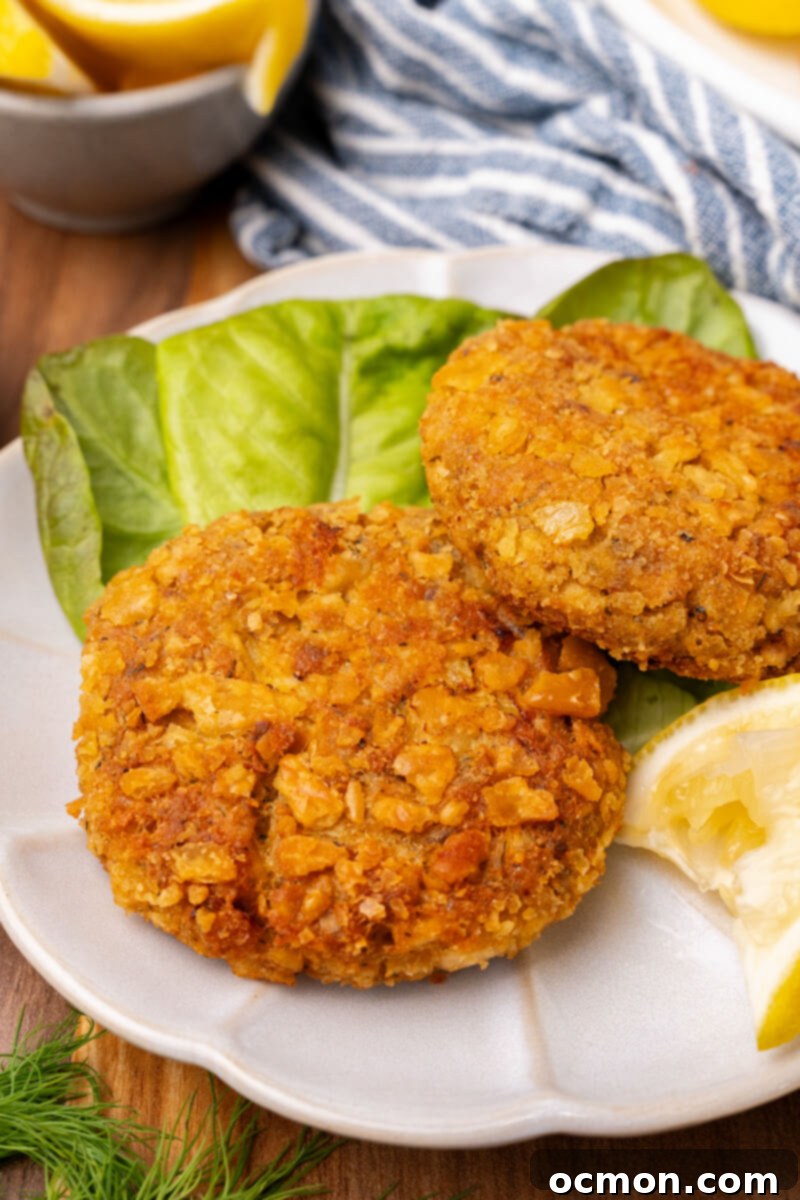 Grandma's Classic Salmon Patties 3 Two salmon patties served on a white plate with a leaf of lettuce and a lemon slice.