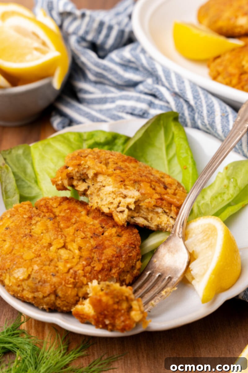 Grandma's Classic Salmon Patties 9 A plate of two salmon patties served with a lettuce leaf and a lemon slice. One of the patties is half eaten, and a fork takes a bite sized piece from the plate.