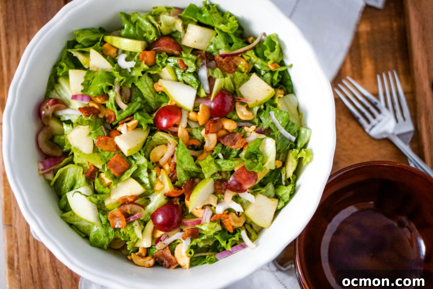 Zesty Cashew Crunch 2 A white bowl of Cashew Nut Salad next to a brown bowl and two forks, showcasing the vibrant ingredients and inviting presentation.