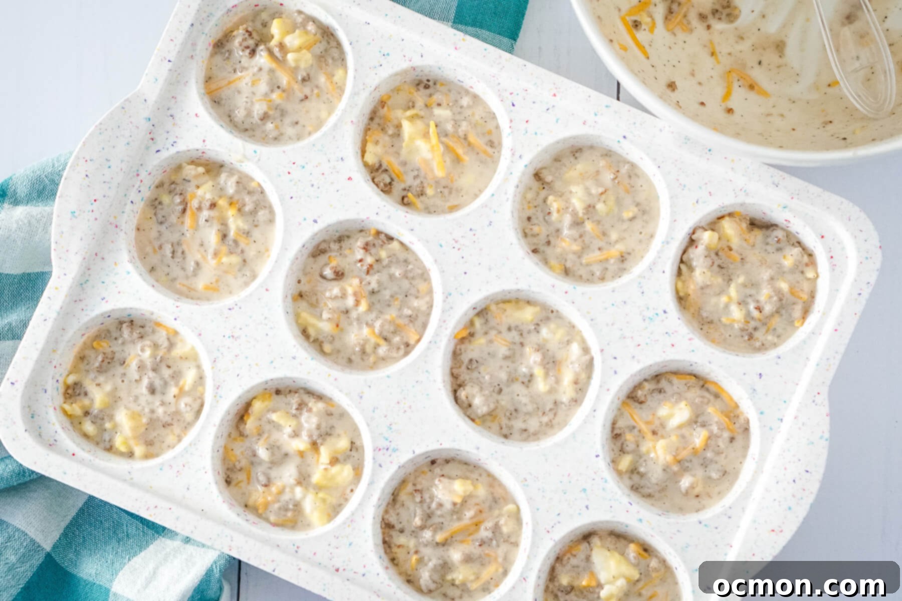 The muffin mixture is added to the greased muffin tin, filling each cavity evenly.