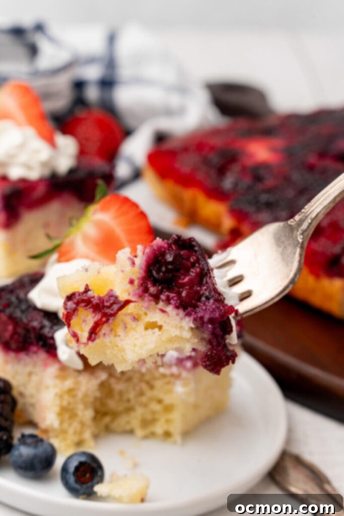 A bite of Berry Upside Down Cake is taken out of the serving and held aloft on a fork.