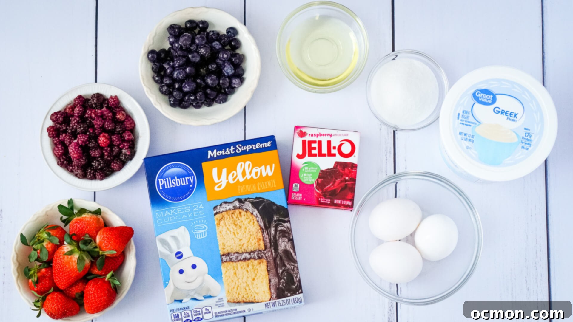 Bowls of strawberries, blackberries, and blueberries, a box of yellow cake mix, a box of raspberry gelatin, three eggs, vegetable oil, sugar, and Greek Yogurt.
