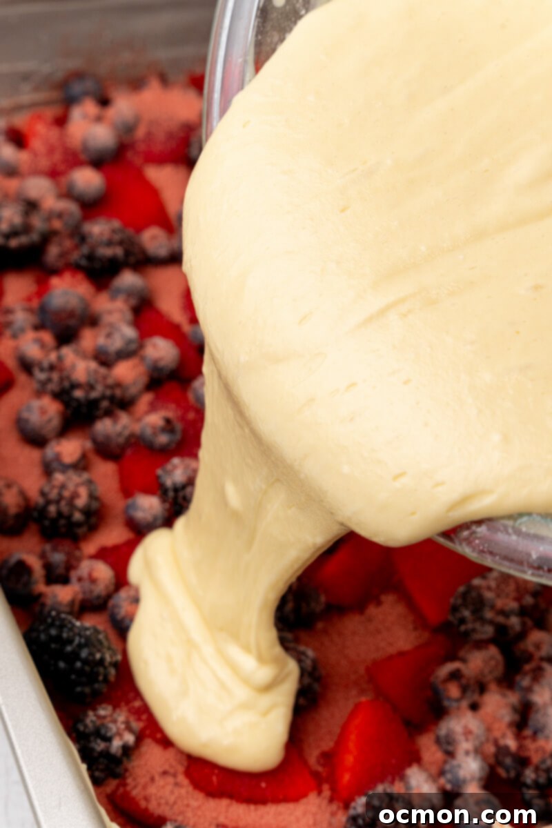 The cake mix is poured evenly over the berries in the pan.