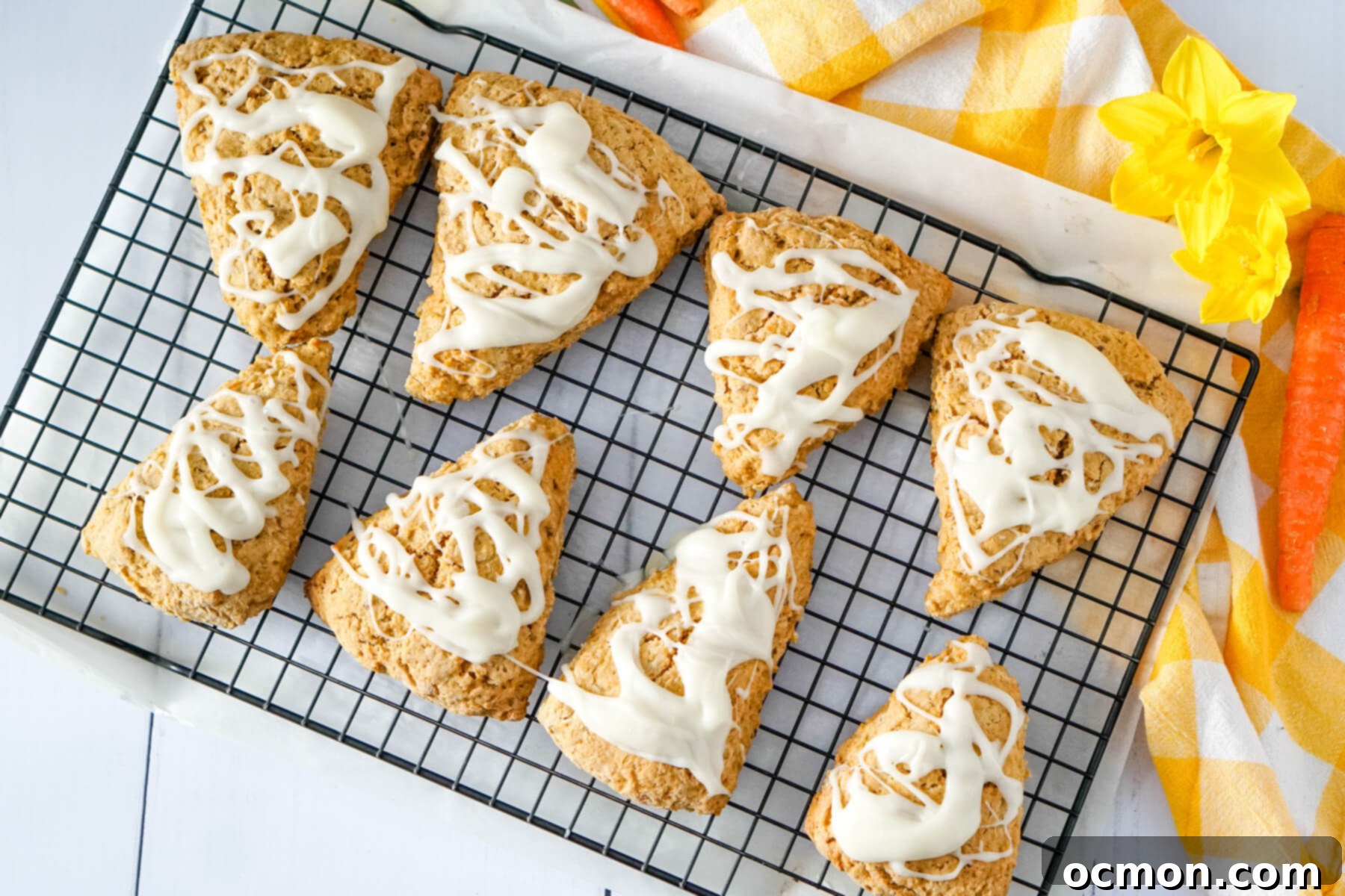A close-up shot of cooled carrot cake mix scones arranged on a wire rack, generously coated with a creamy, white cream cheese glaze.