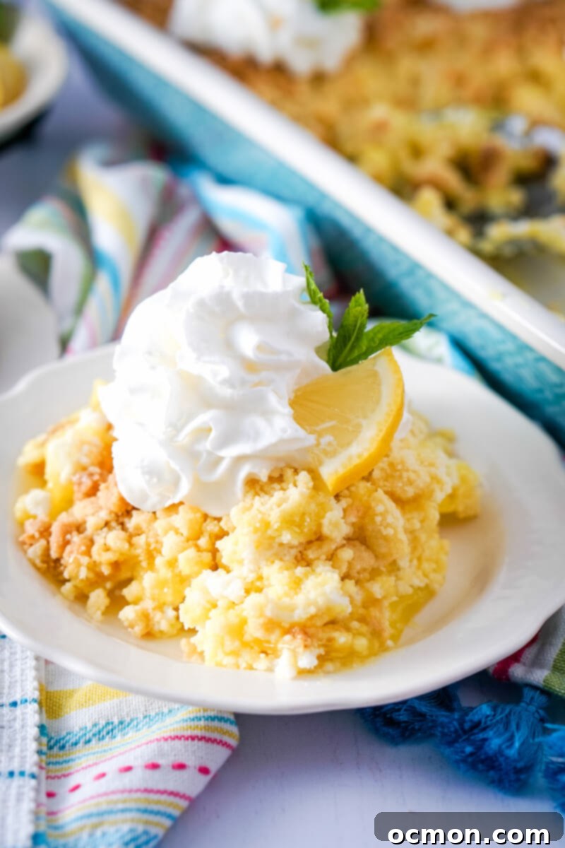 Bright Lemon Dump Cake 2 A generous serving of vibrant lemon dump cake, elegantly topped with fluffy whipped cream, a fresh lemon slice, and a delicate garnish, rests on a pristine white plate.