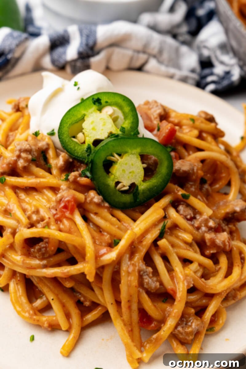 A vibrant close-up of a serving of Cheesy Taco Spaghetti, perfectly topped with fresh cilantro, sour cream, and jalapeños, showcasing its rich texture.