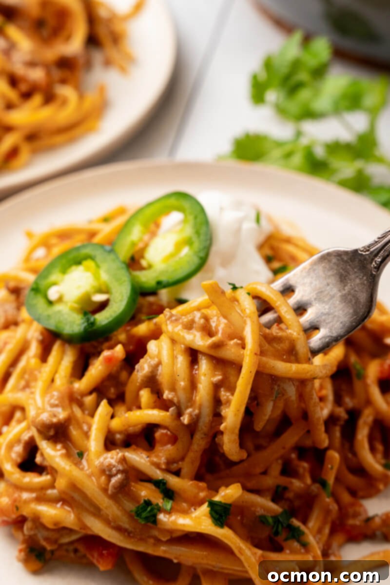 A fork is poised to take a delicious bite out of a heaping serving of Cheesy Taco Spaghetti, showcasing the rich, creamy texture and hearty ingredients.