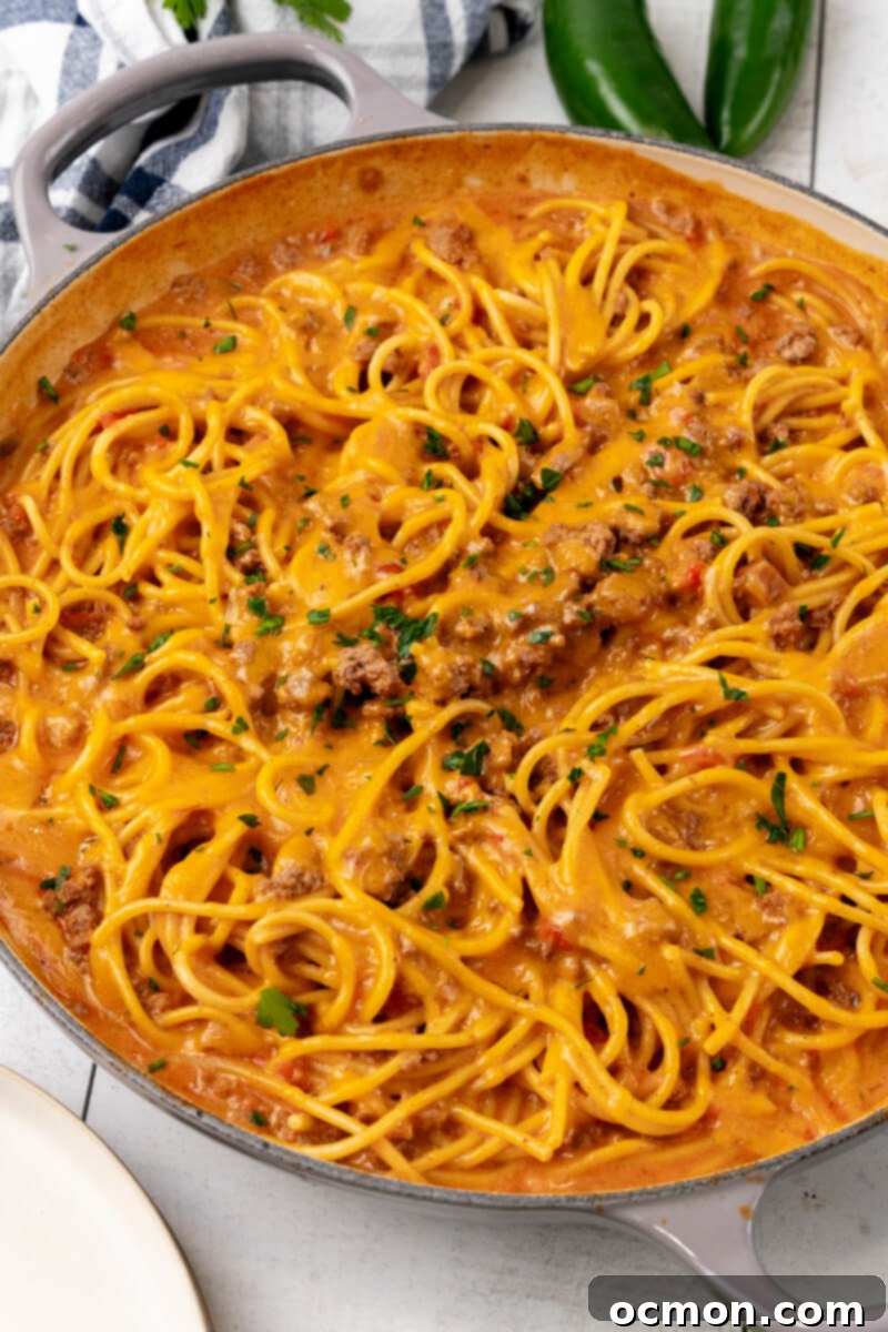 A large skillet brimming with steaming, cheesy taco spaghetti, generously garnished with freshly chopped cilantro, ready to be served.