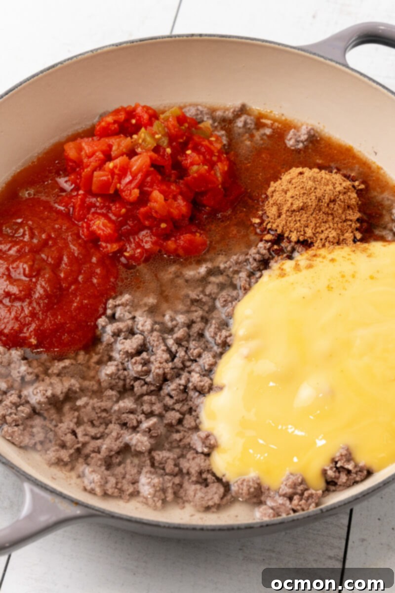 Various sauce ingredients, including taco seasoning, water, cream of chicken soup, Rotel, and taco sauce, are being added to the skillet with the ground beef, beginning to form the rich sauce.