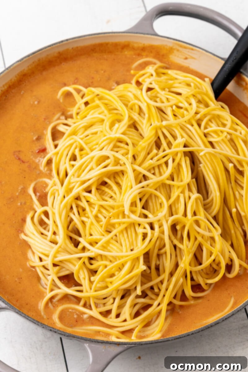 The cooked spaghetti noodles are carefully added to the skillet filled with the rich, cheesy taco meat sauce, ready to be thoroughly mixed.