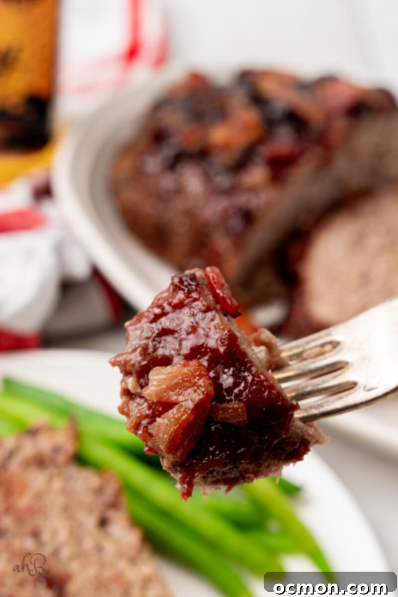 A single fork holds a mouth-watering bite of Bourbon Bacon Meatloaf, showcasing its texture and glaze.
