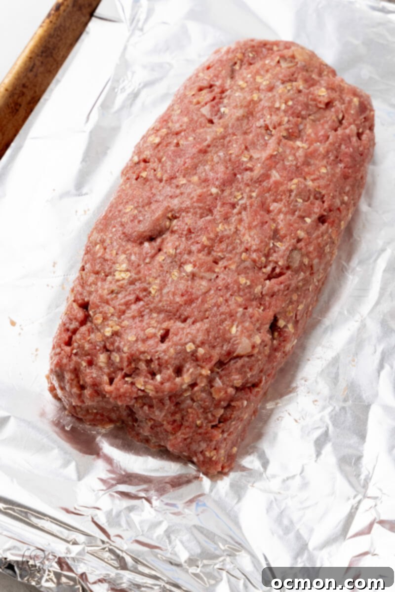 The formed meatloaf, shaped into a neat rectangle, is carefully placed on a foil-lined baking tray, ready for glazing and baking.
