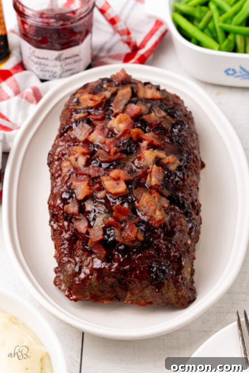 The beautifully golden-brown finished Bourbon Bacon Meatloaf is presented on a pristine white platter, glistening with glaze and ready to be carved.
