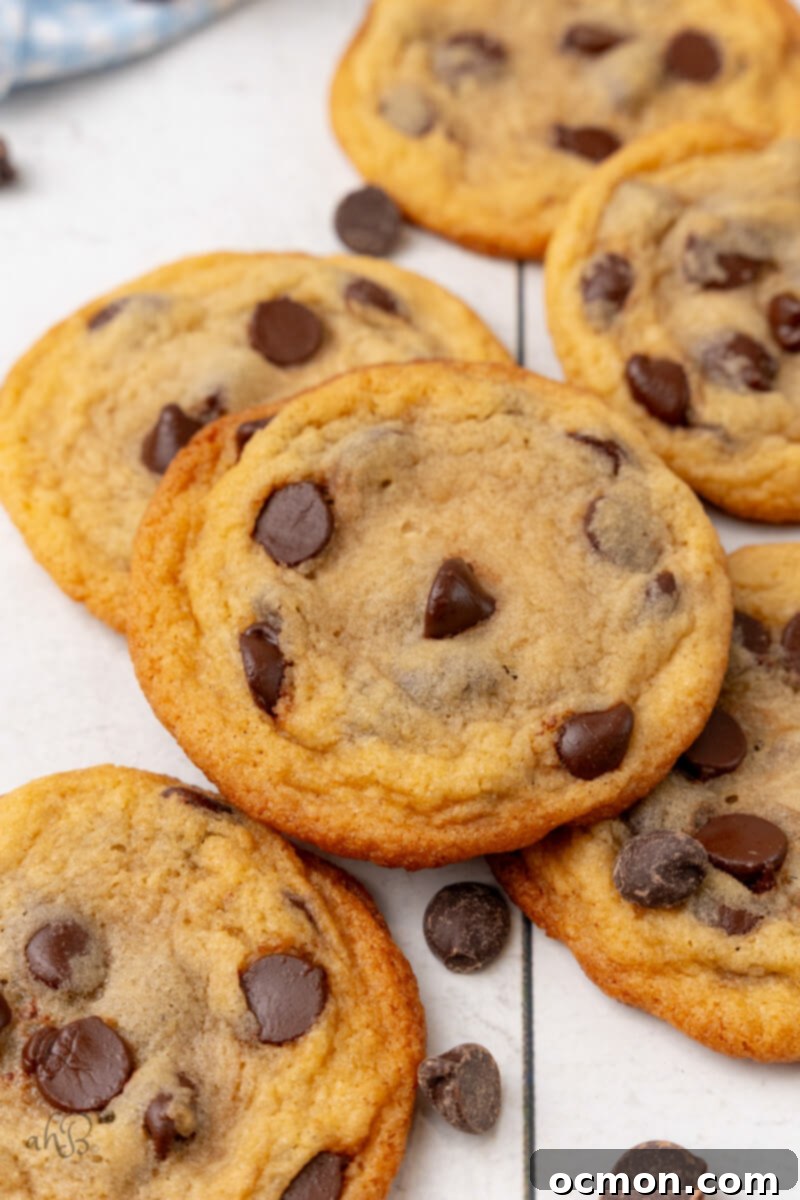 A pile of freshly baked Malted Chocolate Chip Cookies cool on a table, showcasing their golden edges and melty chocolate chips.