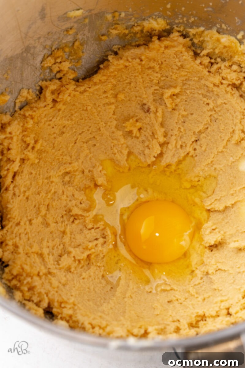 A large egg is carefully cracked and added to the creamy wet ingredients in the mixing bowl, ready to be incorporated.