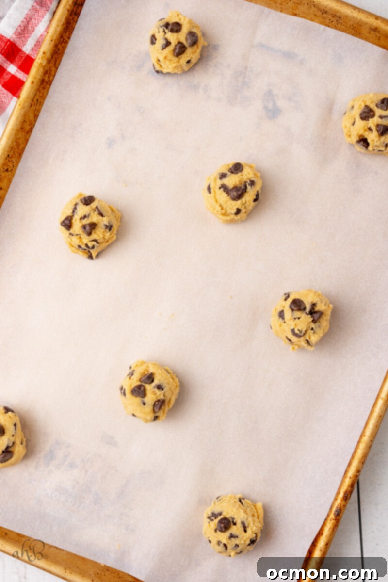 Perfectly portioned spoonfuls of malted chocolate chip cookie dough are evenly spaced on a baking tray lined with parchment paper, ready for the oven.