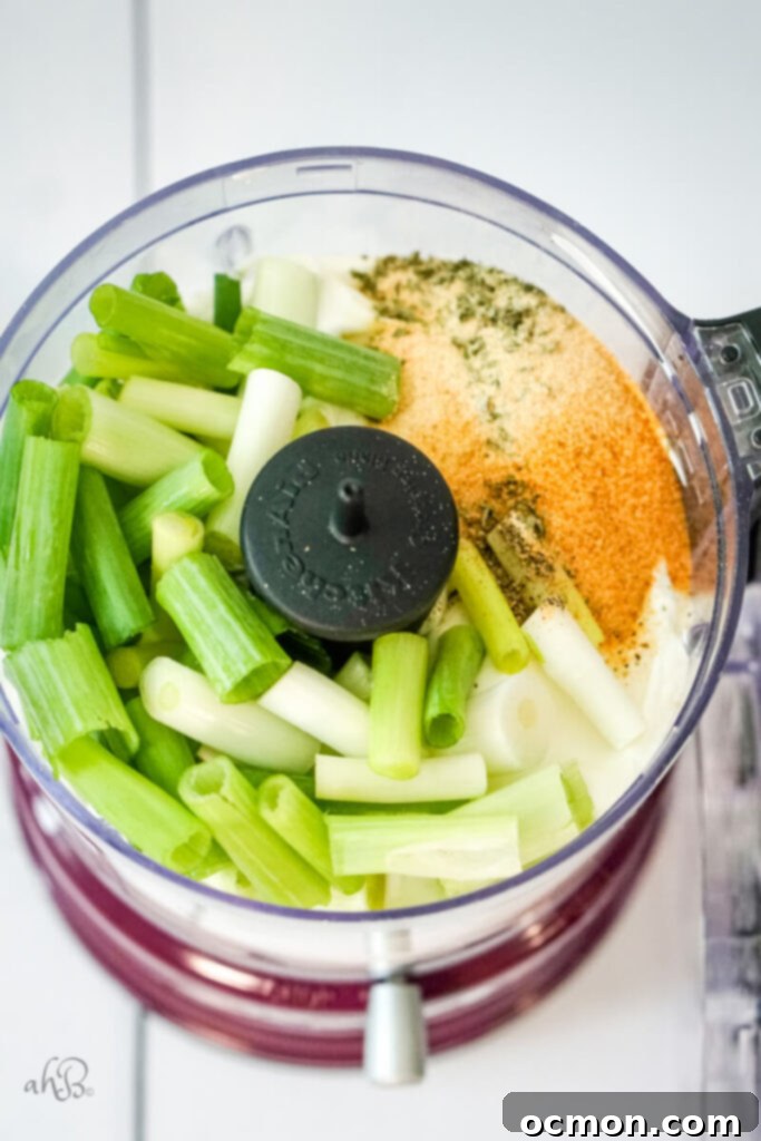 All the green onion dip ingredients, including coarsely chopped green onions, sour cream, and spices, are loaded into a food processor bowl, ready for blending.